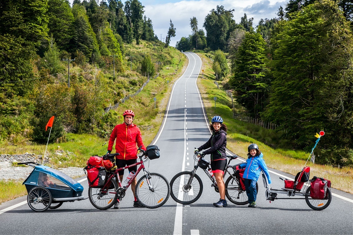 A whole family, kids and all, pose with their bike and trailer set up.