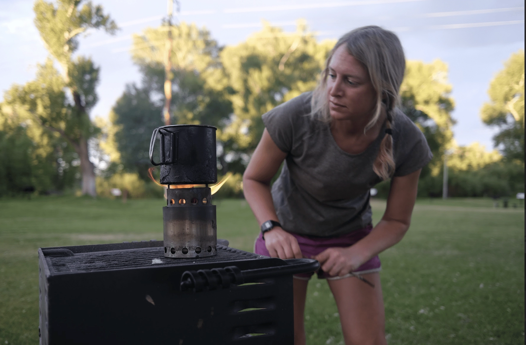 a woman in a park with a twig stove