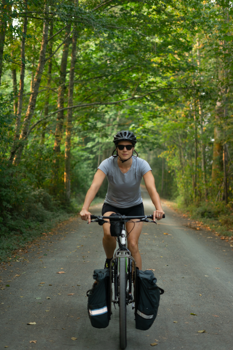 Cyclist wearing clothes for warm weather and sunglasses on gravel trail in the woods.