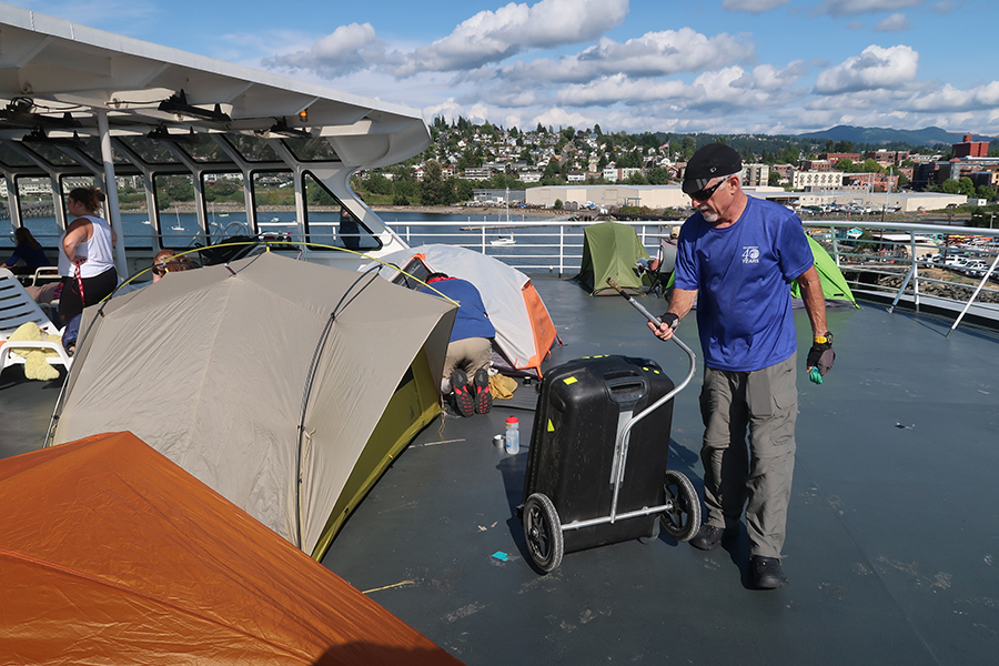 tents set up on the deck of a ferry. A man drags a bicycle trailer.