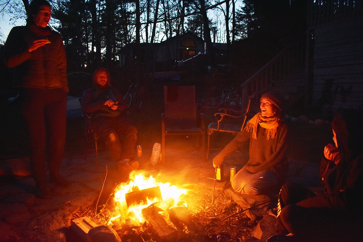 Coworkers sit around a fire at night, their faces lit by the flames.