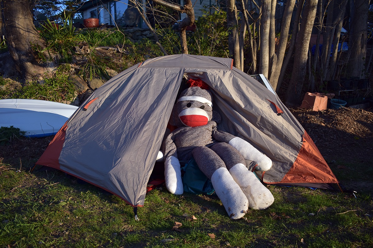 A giant sock monkey sits at the opening of a gray and orange tent.