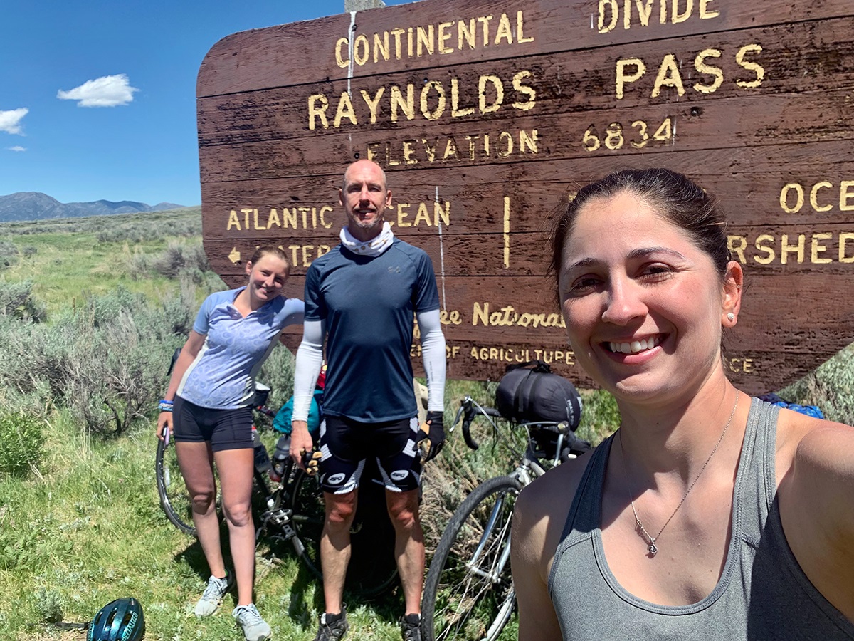 The three companions stand in front of a Continental Divide sign