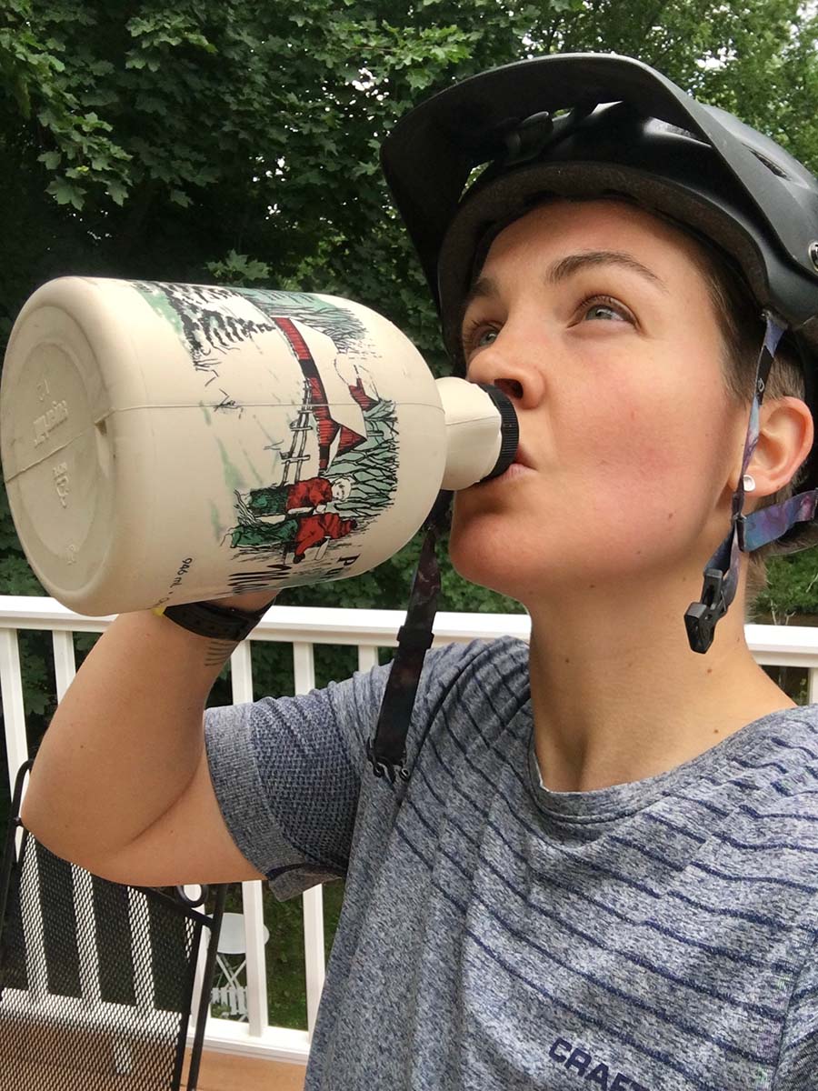 A person in a bike helmet drinks out of a bottle of maple syrup
