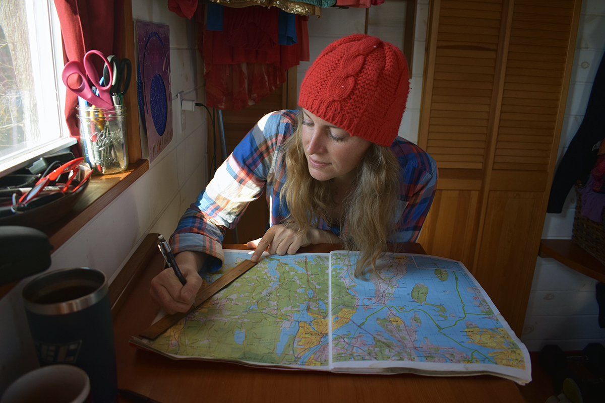 Laura sits in her tiny house with a map in front of her, measuring her area of intrigue.