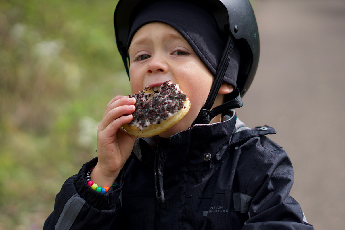 A boy in a helmet eats a giant donut with chocolate sprinkles