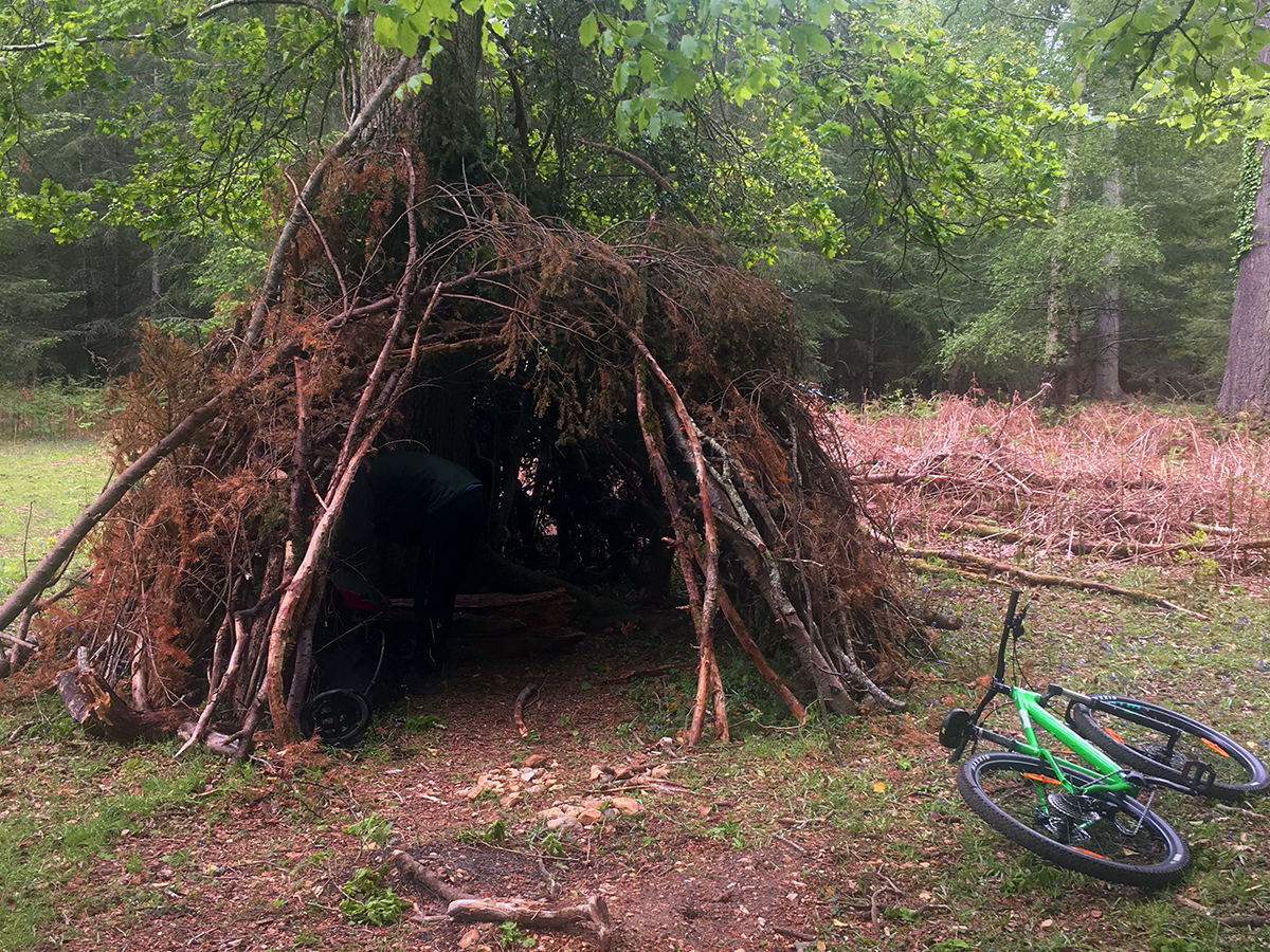 A cone-shaped hut made of branches shelters the riders during their lunch break