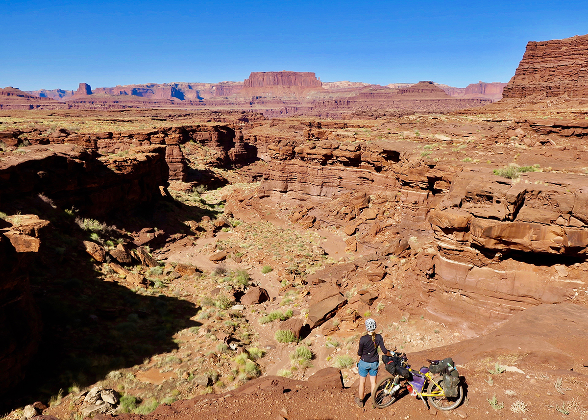 Tara stands with her loaded bike at the edge of a gorge in Canyonlands National Park in Utah.