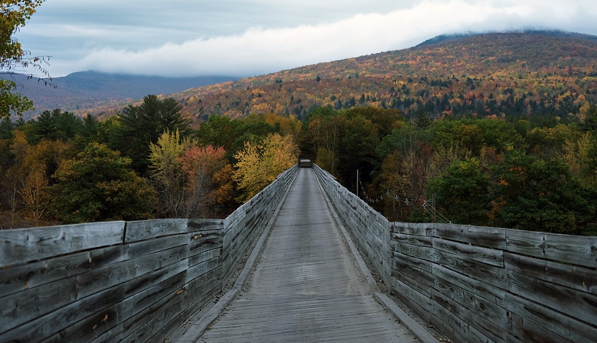 A bridge stretches across a river on the Cross New Hampshire Adventure Route while fall foliage creates a colorful backdrop.