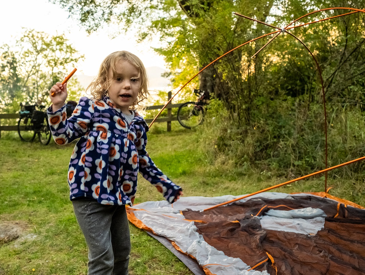 A child walks around the campground as adults are putting up tents around camp.