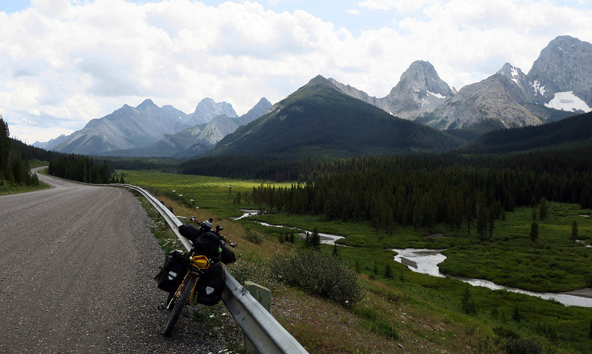 Tara's bike rests against a guardrail on Spray Lakes Road with mountains and a creek in the background