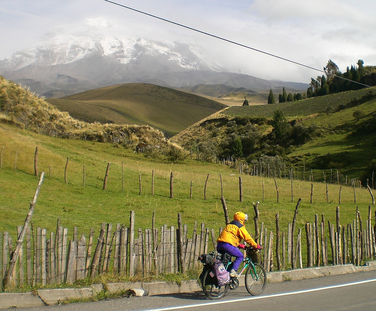 A beautiful view of Laura riding through Colombia after a rain storm, mountains in the background, rain gear on.