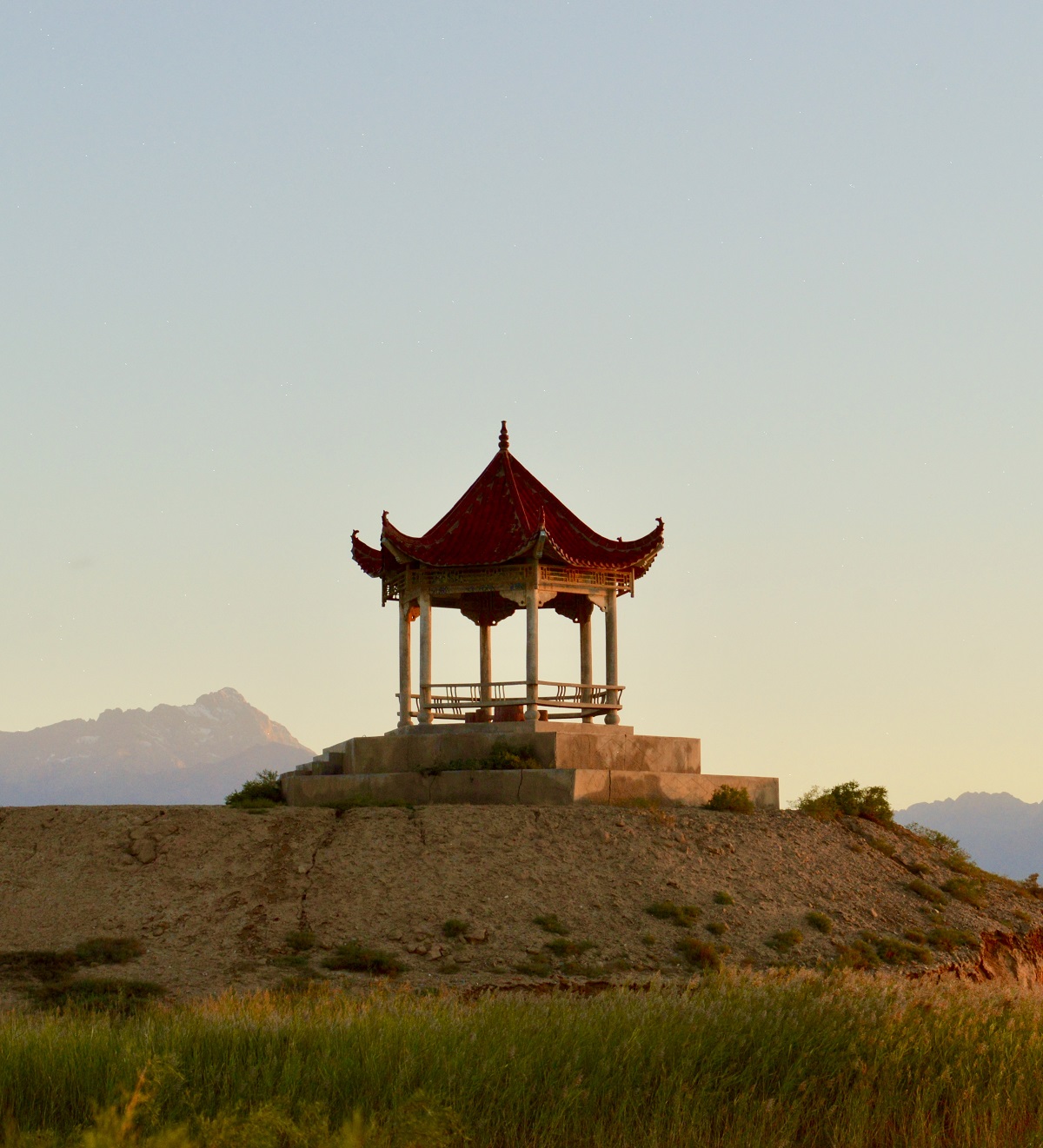 A red pagoda sits on a hill and is backlit by the orange sunrise.