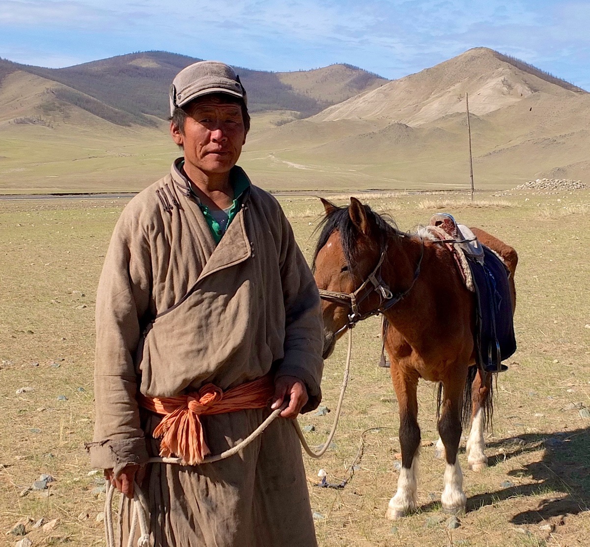 A mongolian man stands with a donkey on a lead for the camera