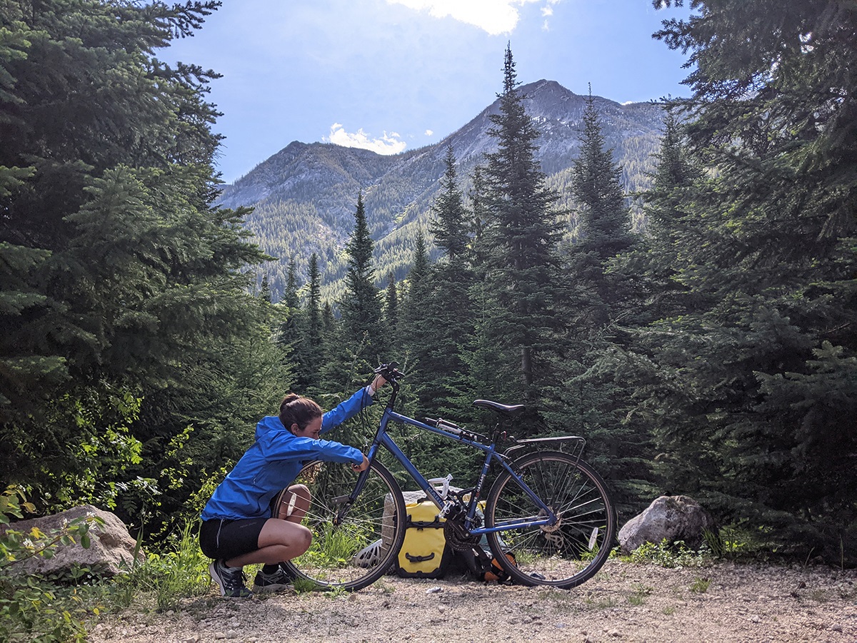 Liliana works on her bike with a big mountain landscape behind her