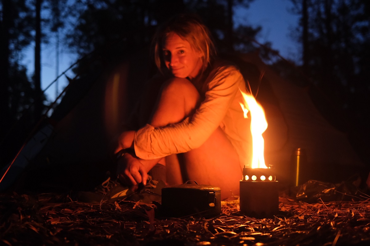 Laura sits in camp in the near darkness, lit by the light of her fire camp stove.