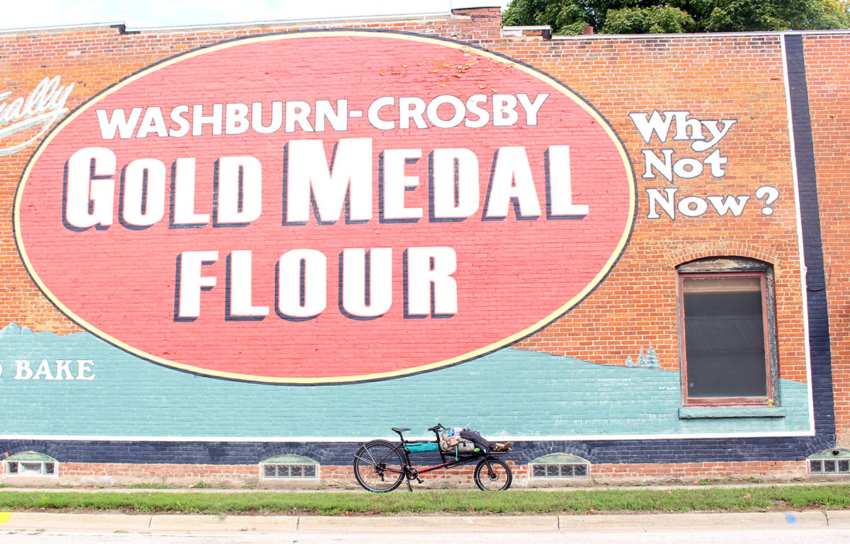 A bike leans against a brick wall painted with a Gold Medal flour advertisement.