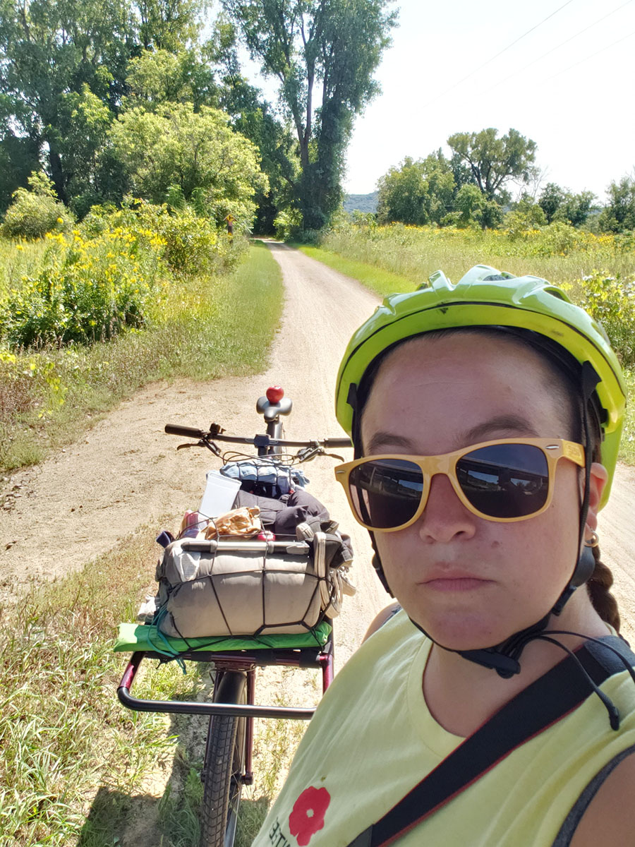 Carmen takes a selfie of them and their cargo bike on the wide, dirt rail trail.