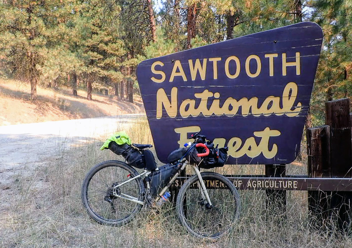a loaded mountain bike leans against a brown national forest sign along a dirt road in the national forest