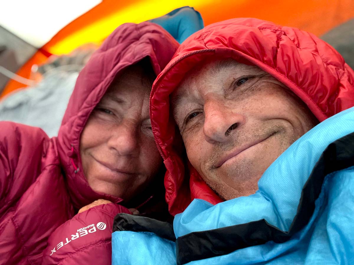 Deb and Tom, two older white people, huddle close in their tent and in their puffy jackets for a selfie.