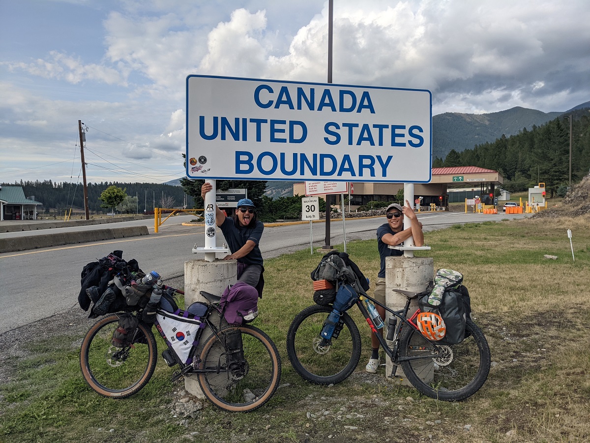 Pak and his friend hug the Canadian border sign, finishing their long adventure.