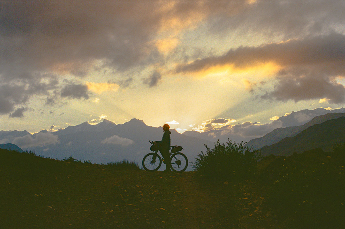 A rider and background mountains are silhouetted against an orange sunset and clouds.