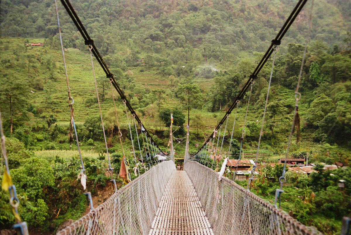 Camera looks directly across a typical Nepalese suspension bridge.