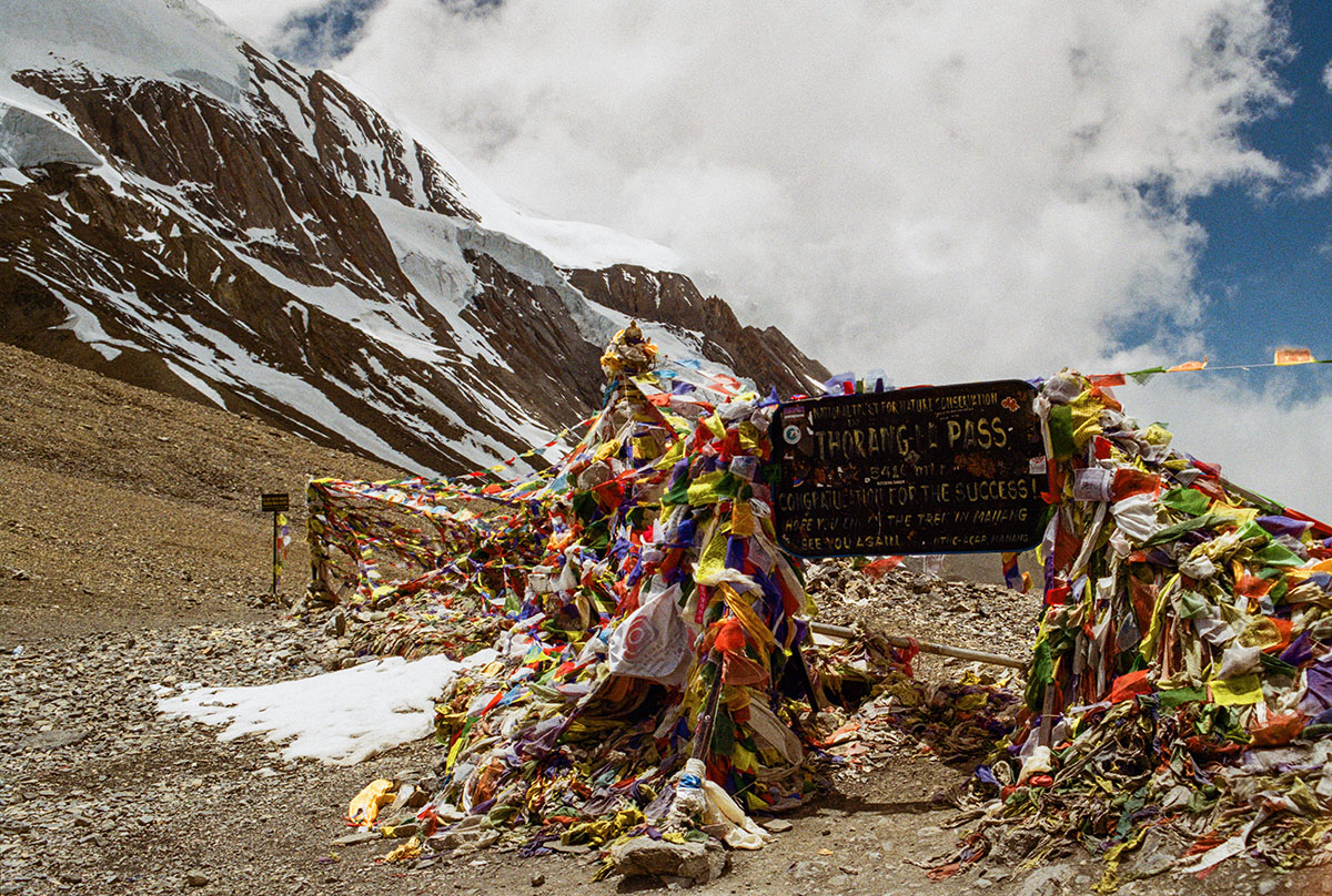 A big sign saying Thorang La Pass has many strands of multicolored Tibetan prayer flags running from its top to the ground.