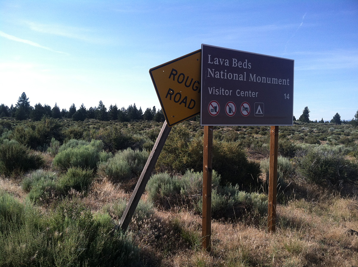 A brown forest service sign that reads Lava Beds National Monument Visitor's Center 14 miles.