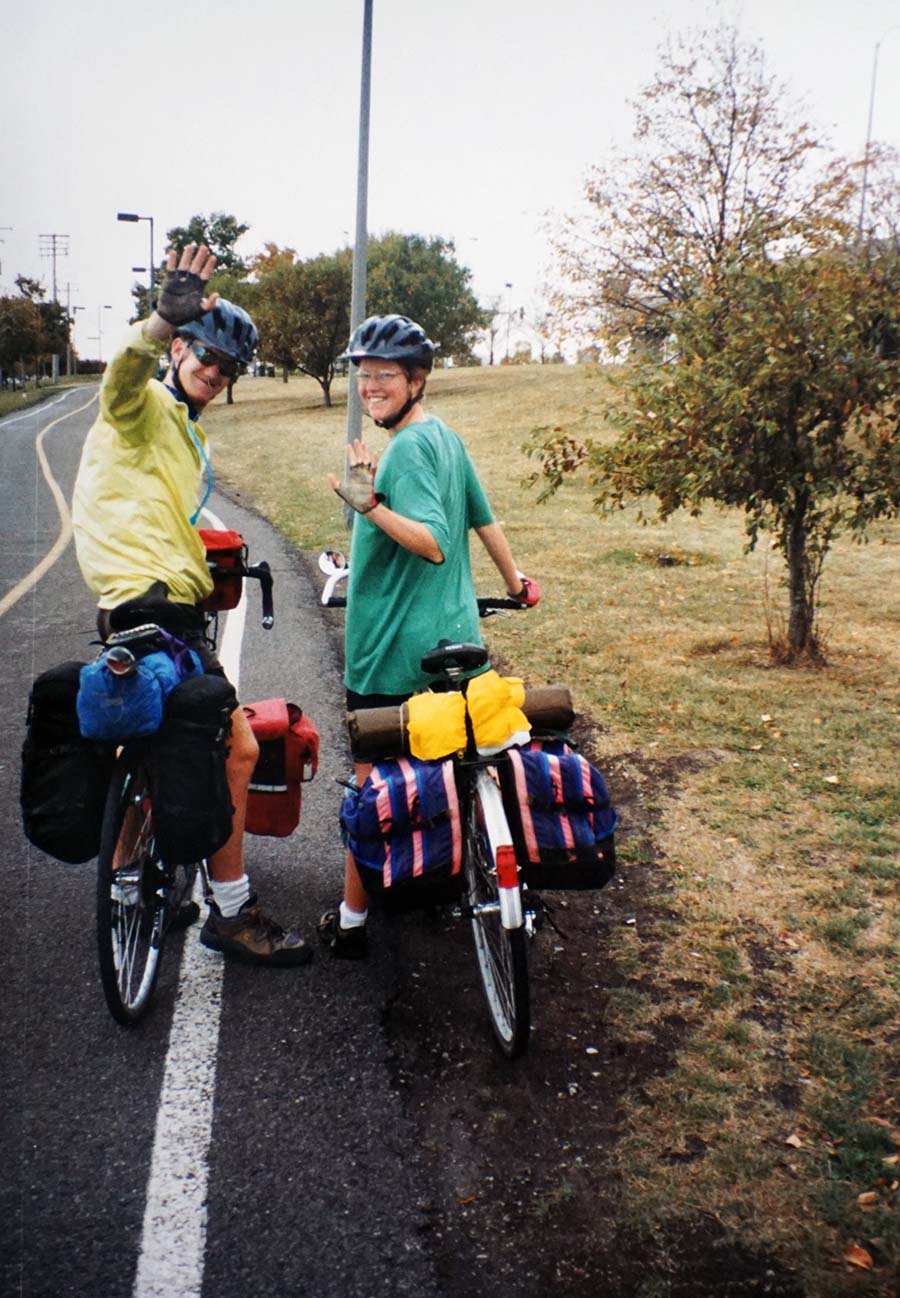 The two younger riders stand over the loaded bikes and look back at the camera, waving goodbye.