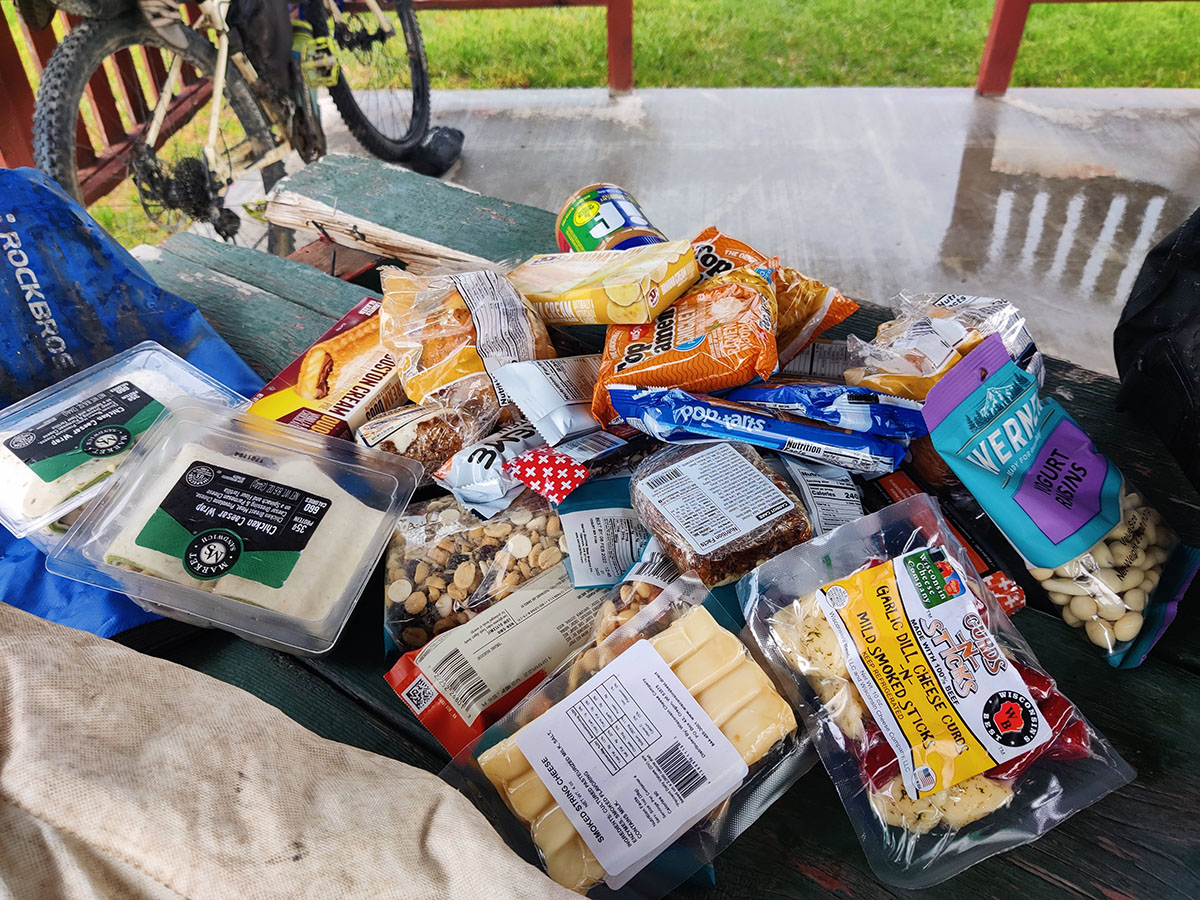 A couple dozen packages of gas station treats - everything from wraps to Pop Tarts - lays spread on an outdoor picnic table.