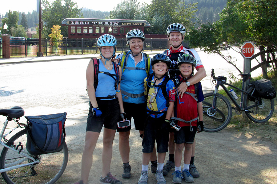 The family of five poses for a photo in their bike helmets at the start of the trail. There is a train caboose in the background.