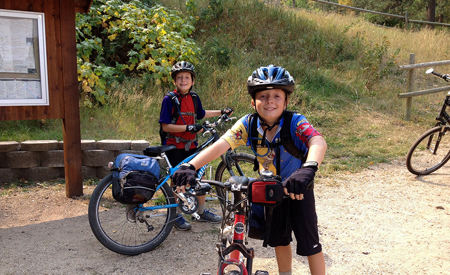 Two little white, brown-haired boys in helmets look tired but happy standing by their bikes on the trail. The boys are ten-year-old twins.