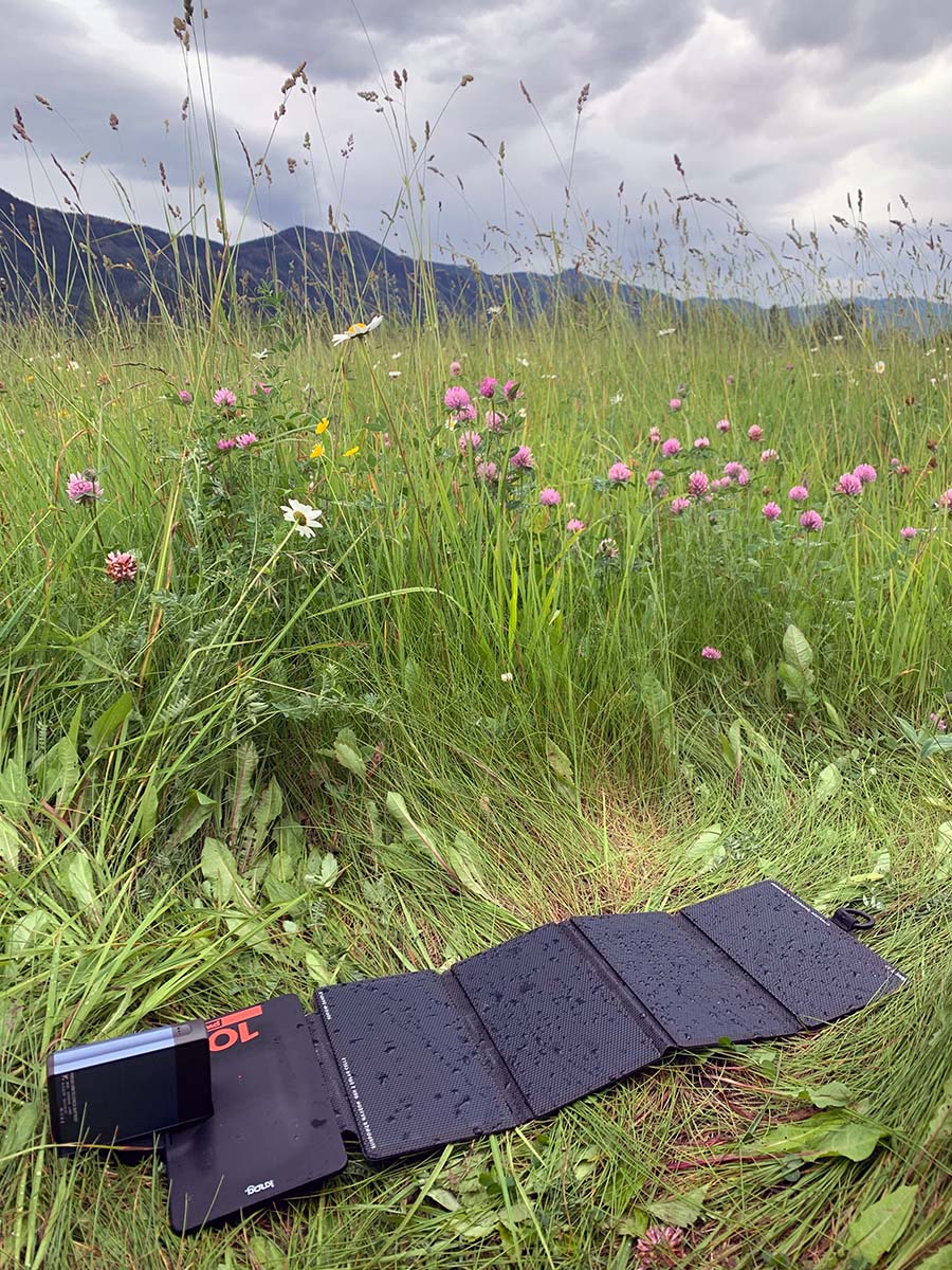 The Knog solar panel lies unfolded in the sun on a field of tall, green grass.