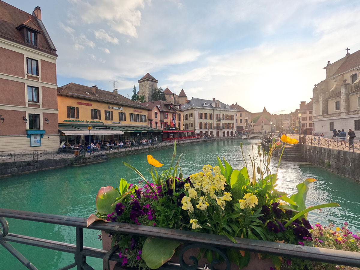 A photo taken from a bridge overlooking a European canal that runs through Annecy, France. Old building line the canal.