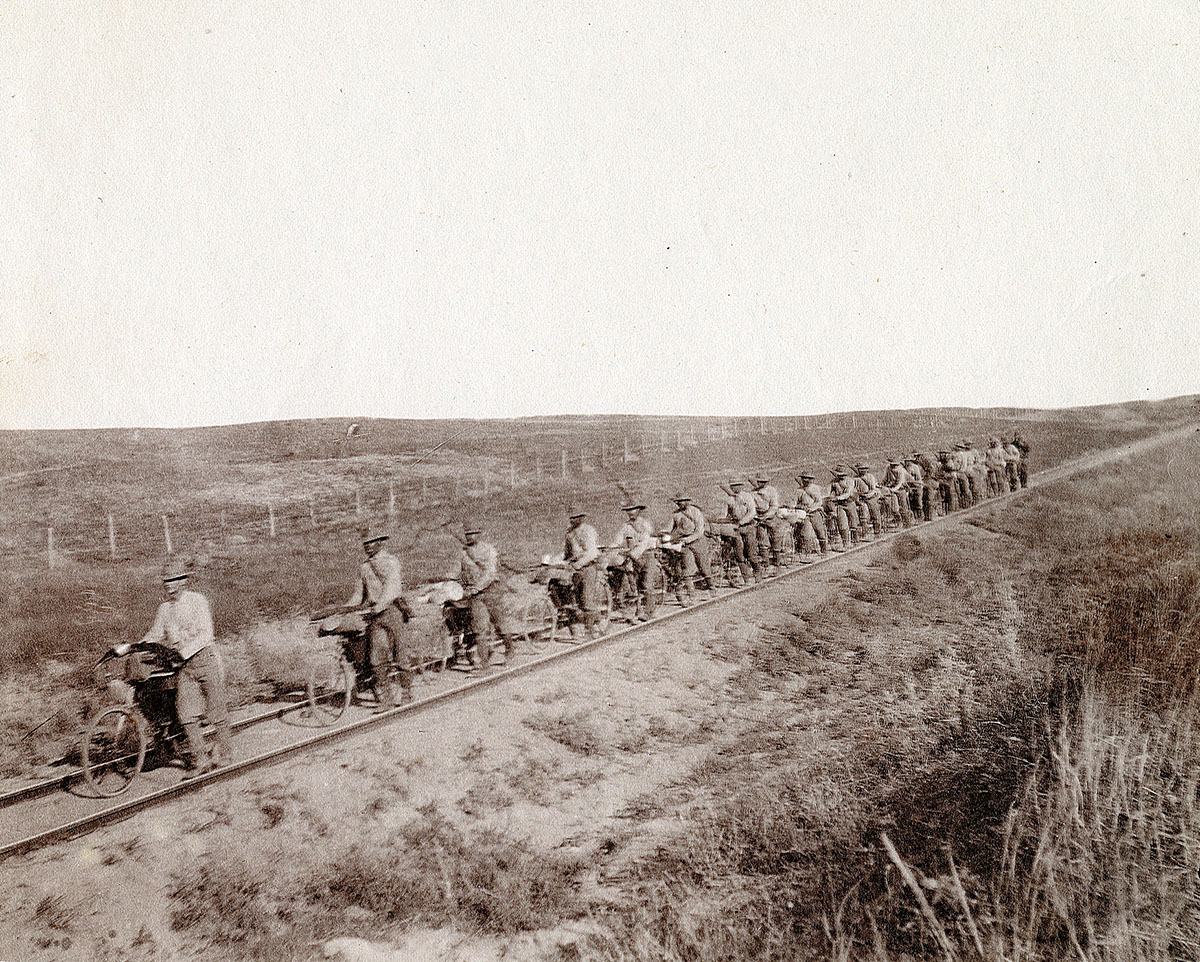 Cyclists line up on a railroad track. The photo is black and white.