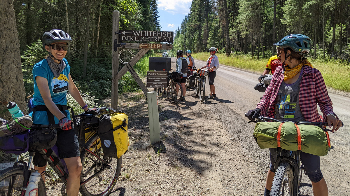 A group of cyclists are stopped and smiling near a sign says Whitefish Bike Retreat and Beer.