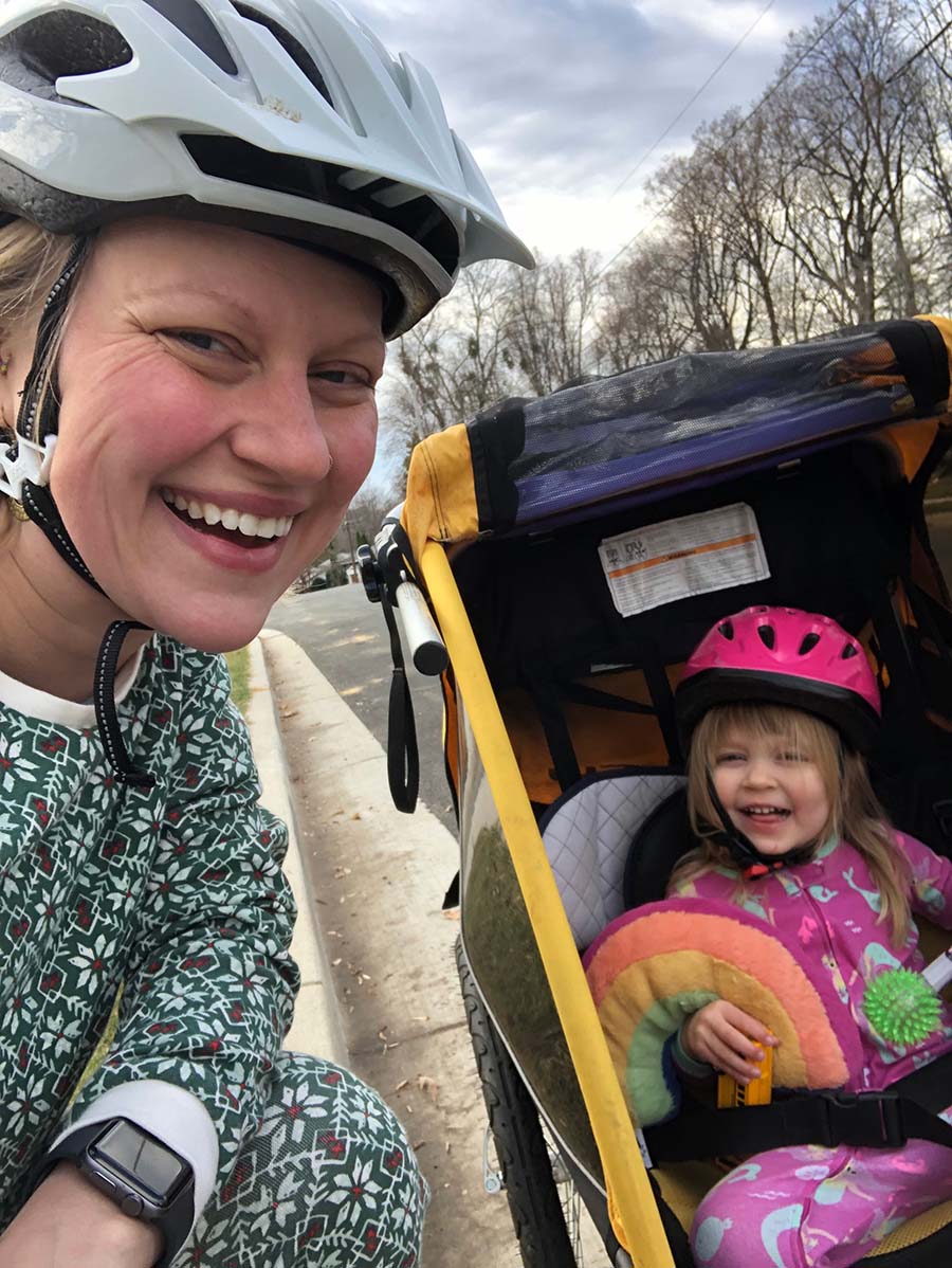 Marissa takes a helmeted selfie with her daughter in a bike trailer. Both are white and blond.