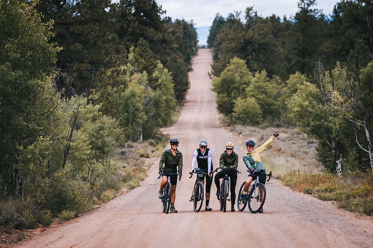 Four of the invited journalists/cyclists stand over their bikes in the middle of a flowy dirt road.