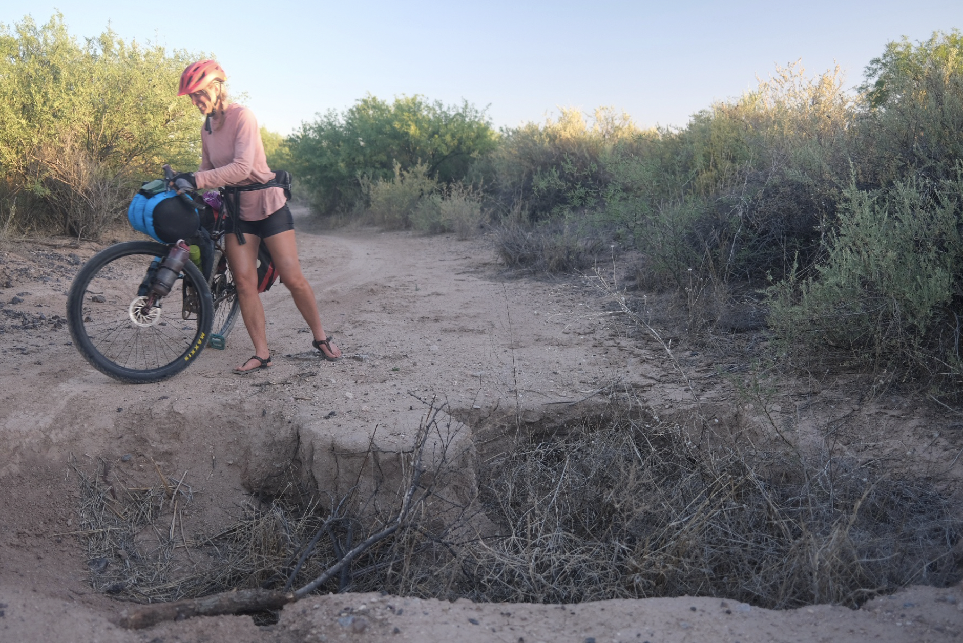 a cyclist pushes her bike on a dirt road