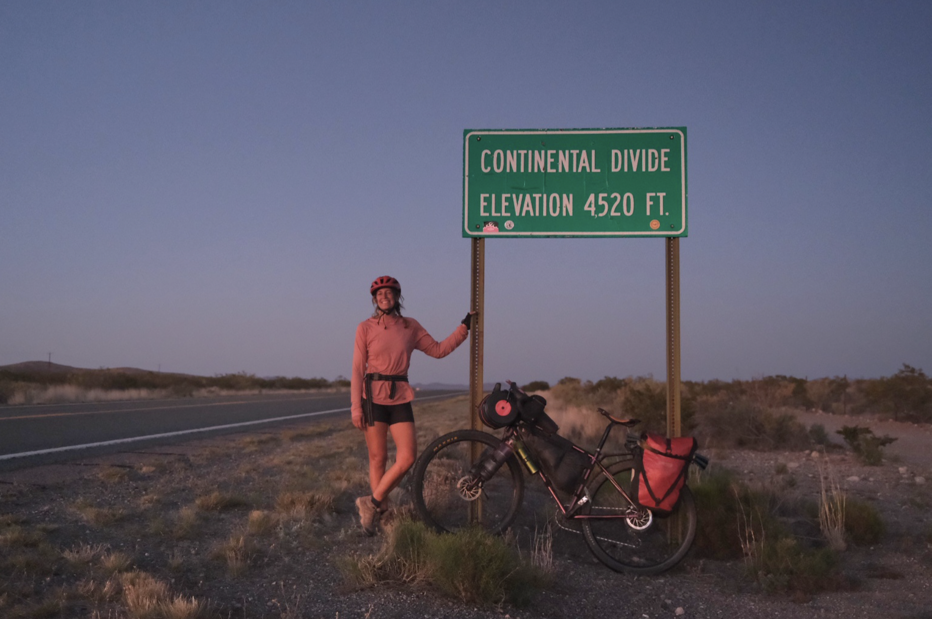a cyclist stands next to a road sign