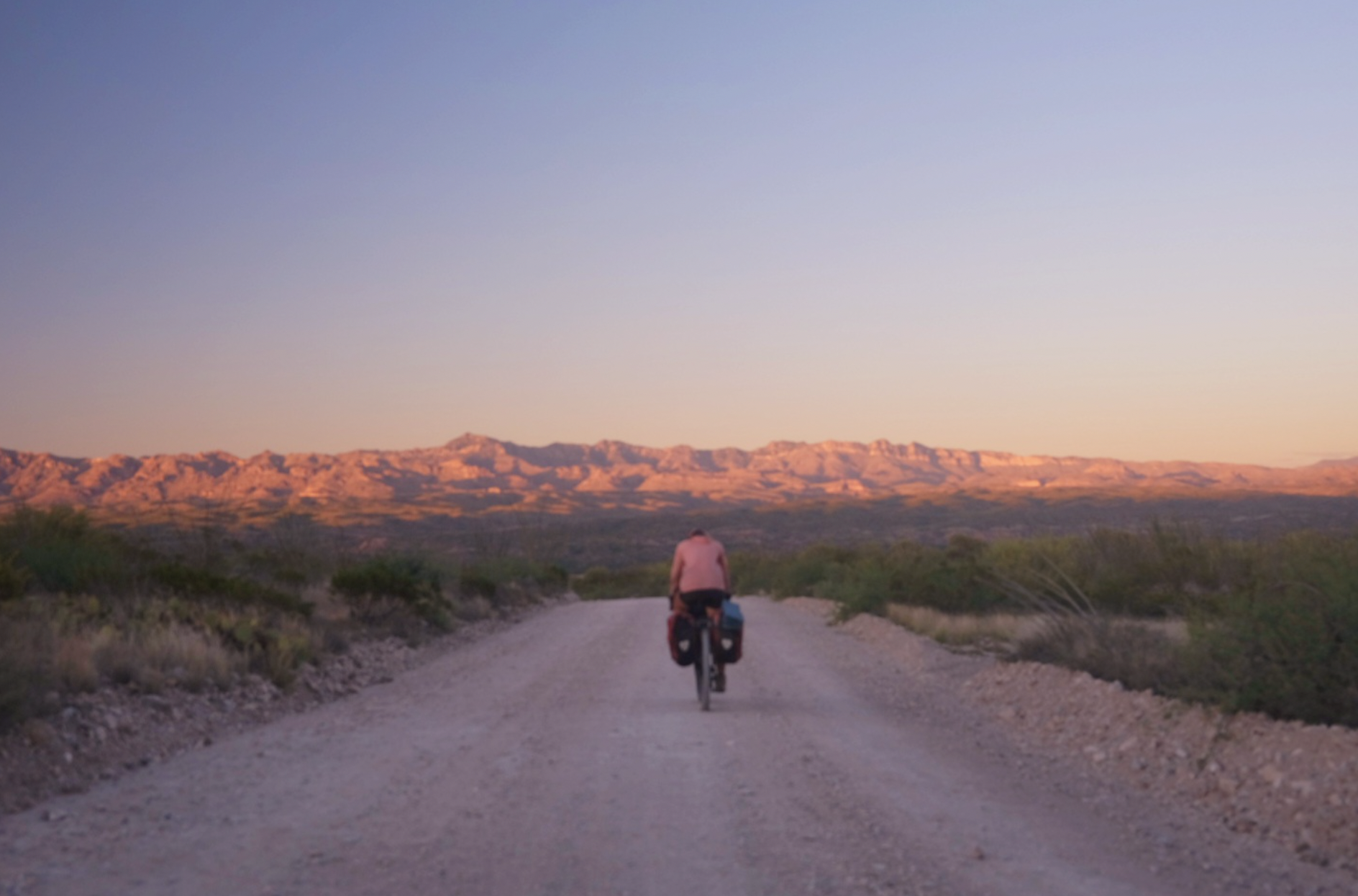 a cyclist rides into a desert sunset 