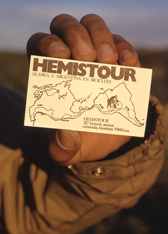 A dirty hand holds a business card with a simple Hemistour map