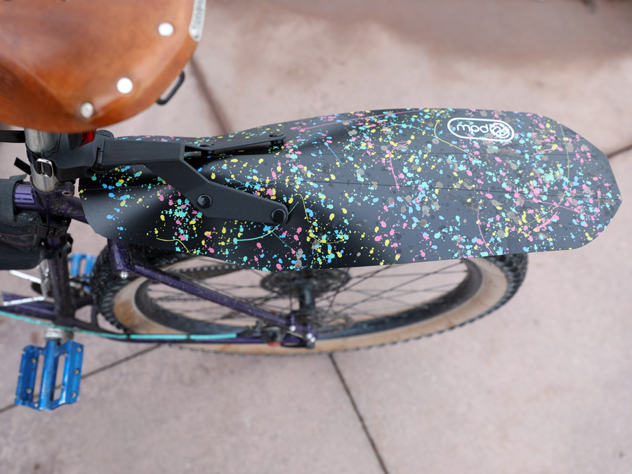 A plastic clip on fender with a paint splatter design below a leather bike saddle.