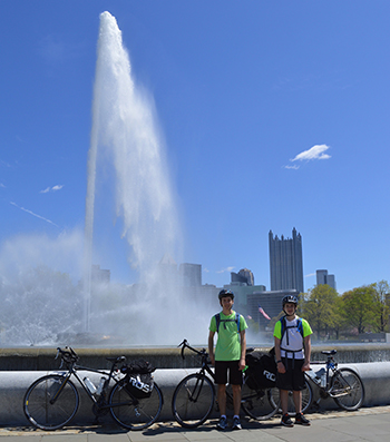 Teenaged boys stand with bikes in front of vertical plume of water.