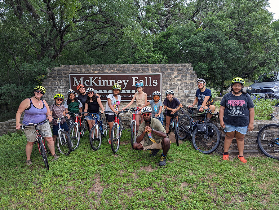 children and a few adults with bikes in front of the stone McKinney State Park sign