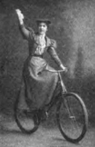 Black and white photo of a woman in Victorian dress on a bicycle