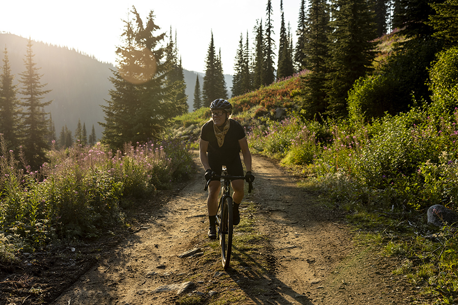 A woman rides the Liv Devote Advanced Pro on a dirt road with fireweed blooming