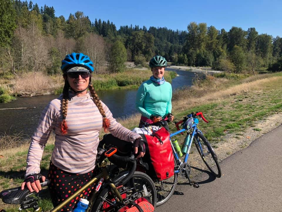 Two women next to their loaded bicycles in front of a river.