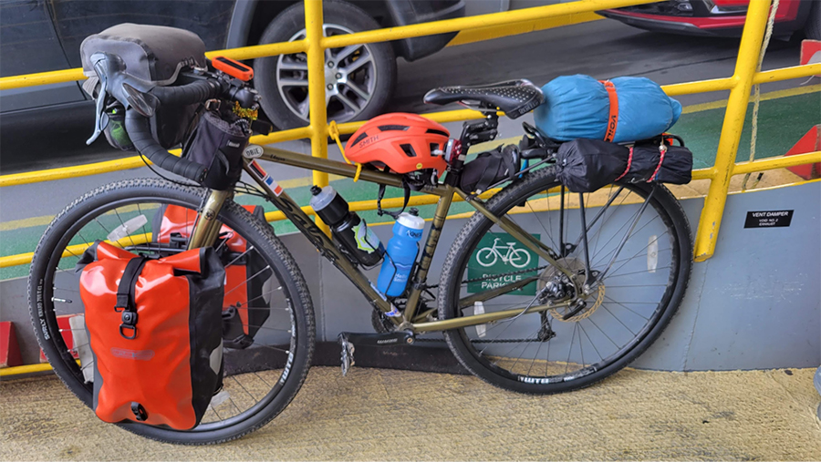 Loaded bicycle against a railing with a sign indicating that this is where bicycles go.